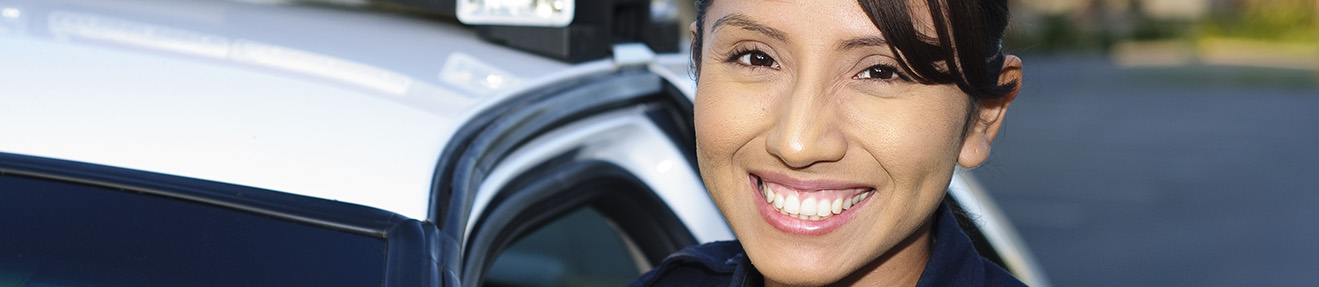 A female law enforcement officer stands in front of a cruiser.